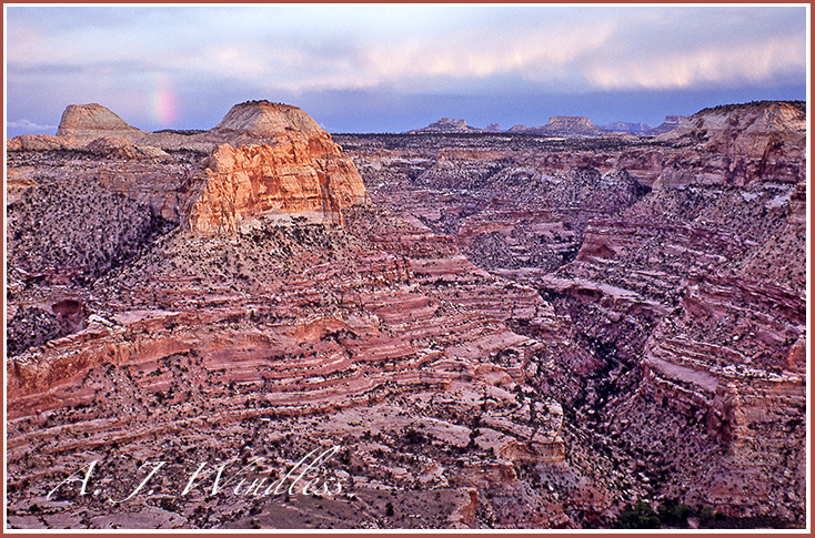 Overlook of the San Rafael Swell with a distant rainbow and glowing rain.