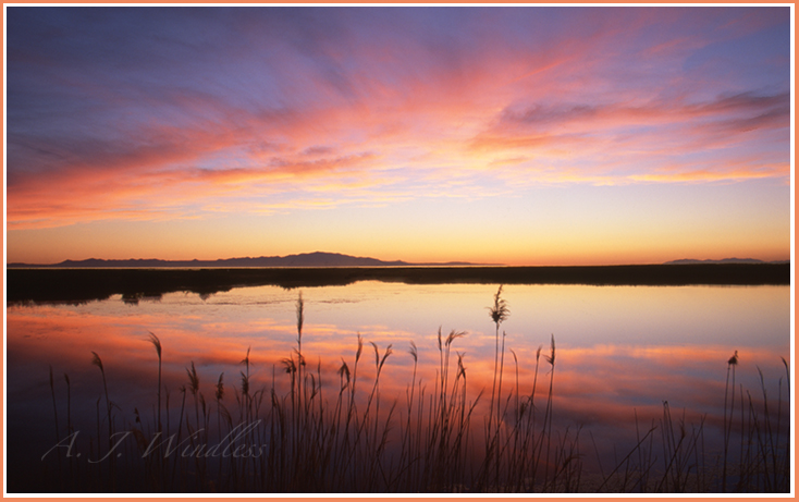 A beautiful sunset reflected perfectly in the foreground lake while the Great Salt Lake shows a sliver of color in the background.