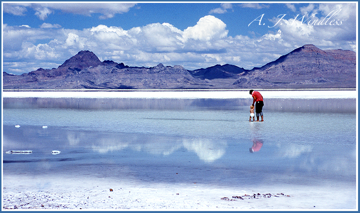 A father wades his baby by the hand through the reflective waters and onto the salt near the Great Salt Lake.