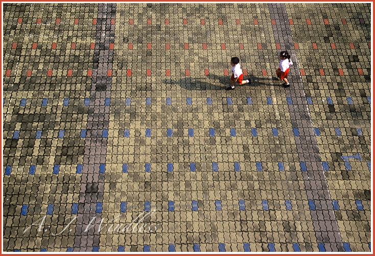Two kindergarten students chase each other around on the colored bricks.