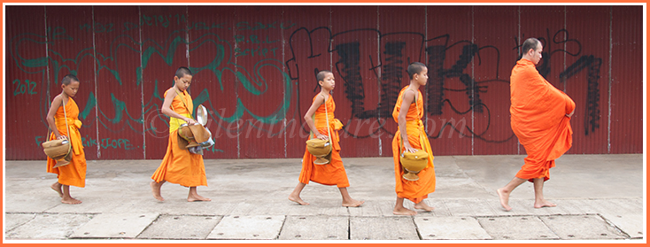 Young Buddhist monks dressed in orange robes walk past the graffiti struck walls