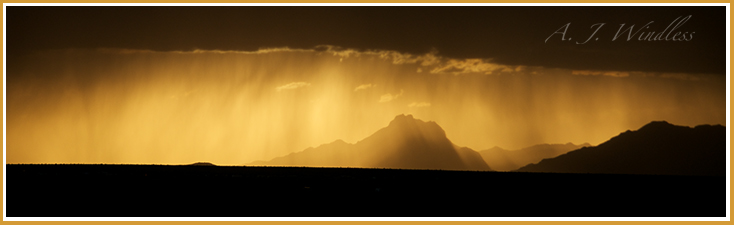 In the distance last sunlight breaks under the clouds and illuminates rain falling across the mountain.